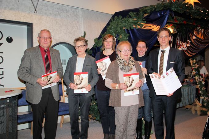 Sechs Personen stehen nebeneinander und halten Broschüren vor weihnachtlicher Dekoration